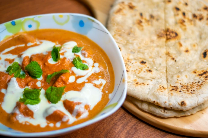 Chicken tikka masala with naan bread on a wooden board.